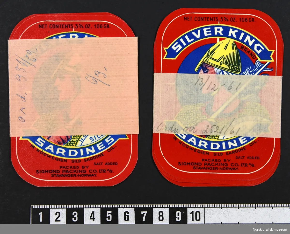 To bunter med etiketter med papirbånd rundt. Etiketten har rød bakgrunnsfarge, og en stor illustrasjon av en langhåret mann i rustning og sverd i en rund ramme midt på. 

"Sardines in Norwegien sild sardine oil"