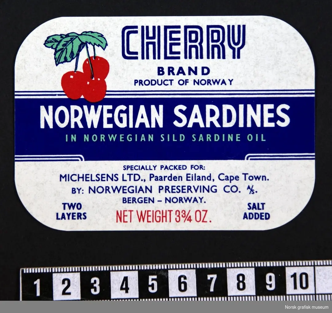 Etikett med hvit bakgrunn og detaljer i blått og rødt. I venstre øvre side er en fremstilling av tre kirsebær. 

"Norwegian sardines in Norwegian sild sardine oli"