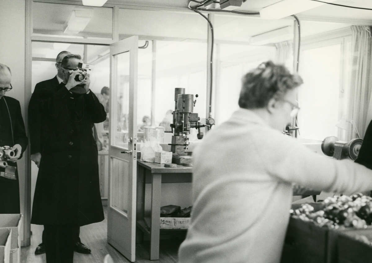 Biskop Bo Giertz besöker den daliga verksamheten på Stretereds vårdhem och skola i samband med Biskopsvisitationen år 1966. En man fotograferar en person i arbete.