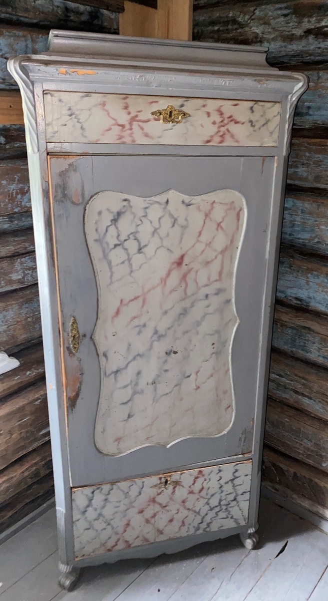 Skuffene og dørspeilet er marmorerte. 2 hyller, pluss skjehylle. Messingbeslag på døra og på begge skuffene. Litt utskåret på beina og øverst på sidene over frambeina.