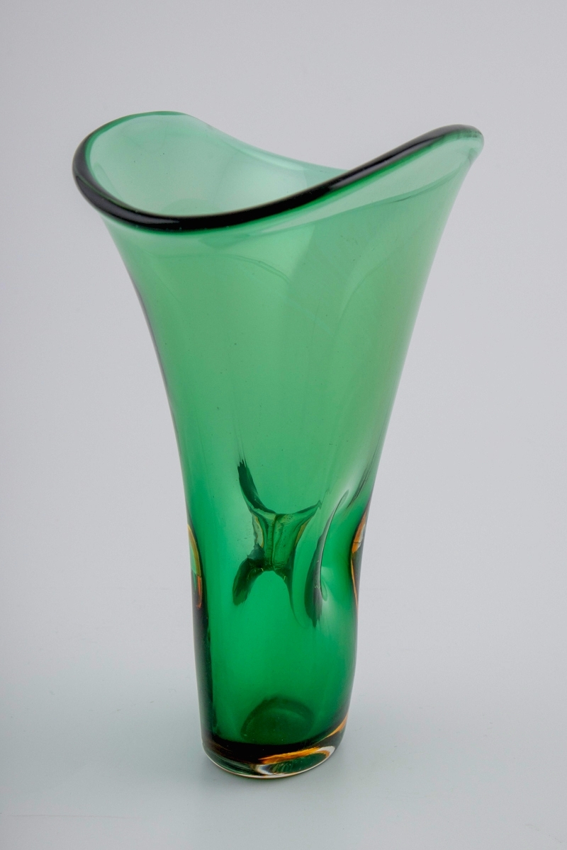 Grønnfarget vase i gjennomskinnelig glass. Vasen hviler på en ovalformet bunn, som er utført i gulbrunt og klart glass i overfangsteknikk. Fra den smale bunnen reiser vasens vegger seg i en bred vifteform, hvor langsidene er forbundet med et gjennomgående hull i midten. Ujevn ovalformet munningsrand.