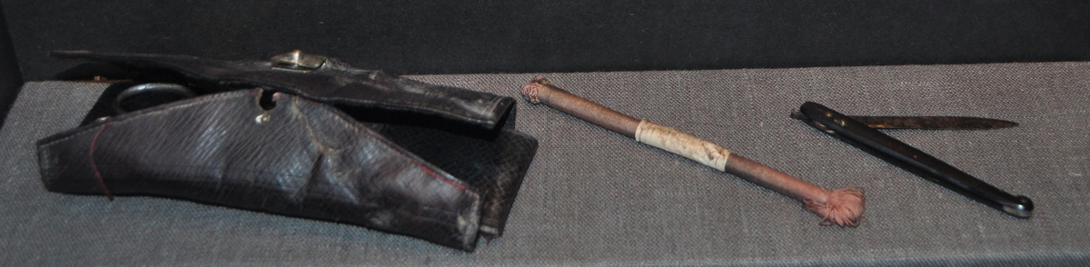 Ett fodral innehållande: sax, kniv med ett svart hornskaft samt en rulle med silke.