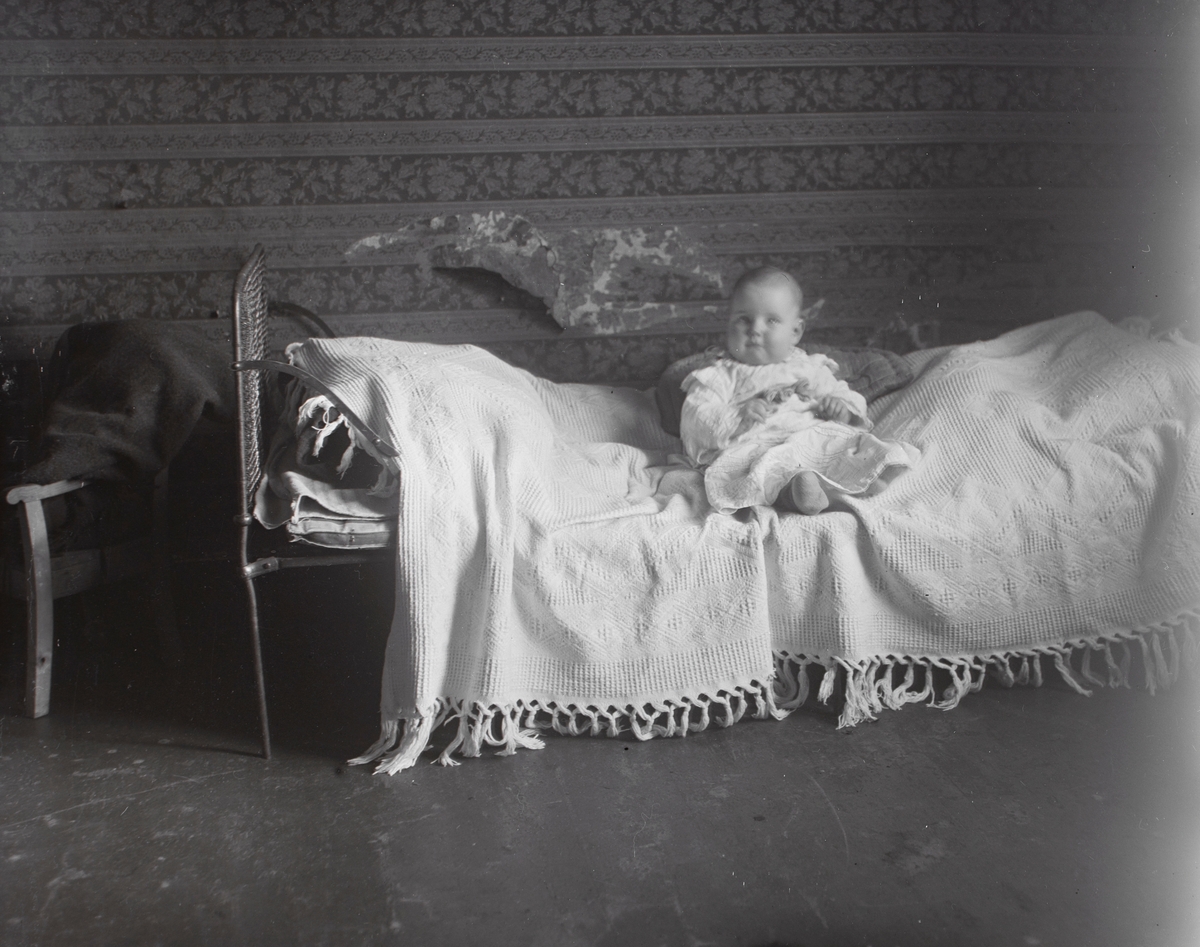 Portrett av en baby som sitter i ei seng.