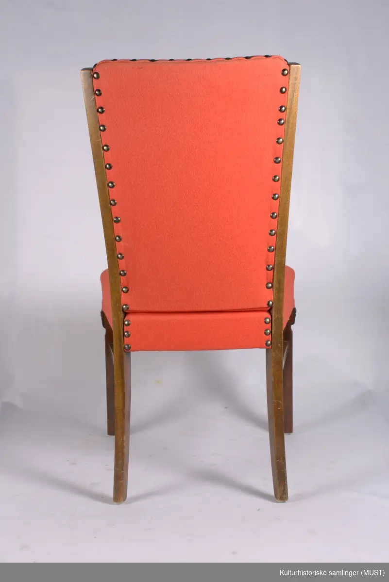 Spisestuestol med sekundært rødt trekk. Stoppet rygg og sete. Frambein formet som korintiske kapitel.