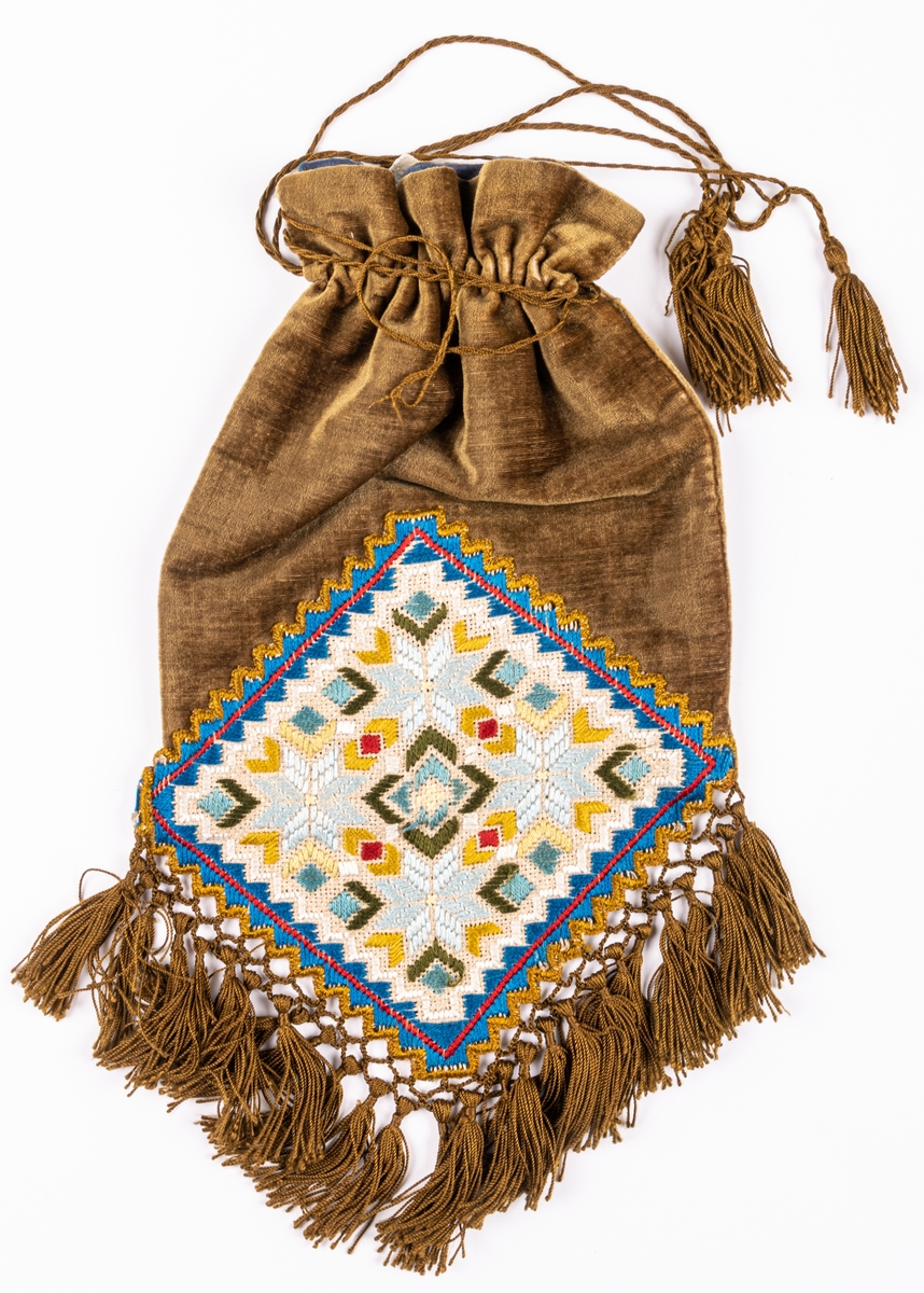 Väska av mossgrönt sammet, påsmodell, frans av bronsfärgat silke och broderi på stramalj.
Från början av 1900-talet.