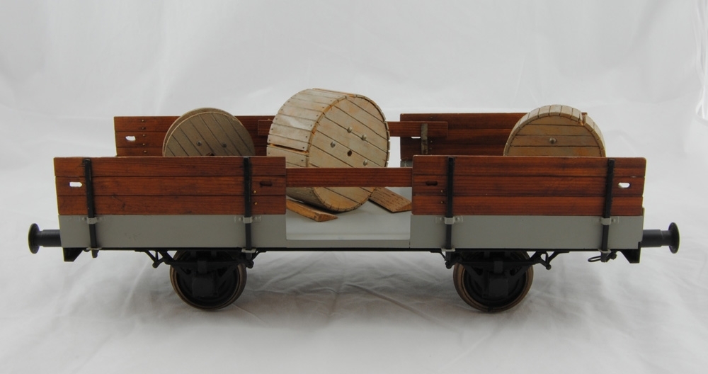 Upplagsvagn, skala 1:20. Öppen vagn med tre kabeltrummor (Jvm 12173:2-4) och fem träkilar som håller dem på plats (Jvm 12173:5-9. Tillhör montagetåg för kontaktledningsarbete.