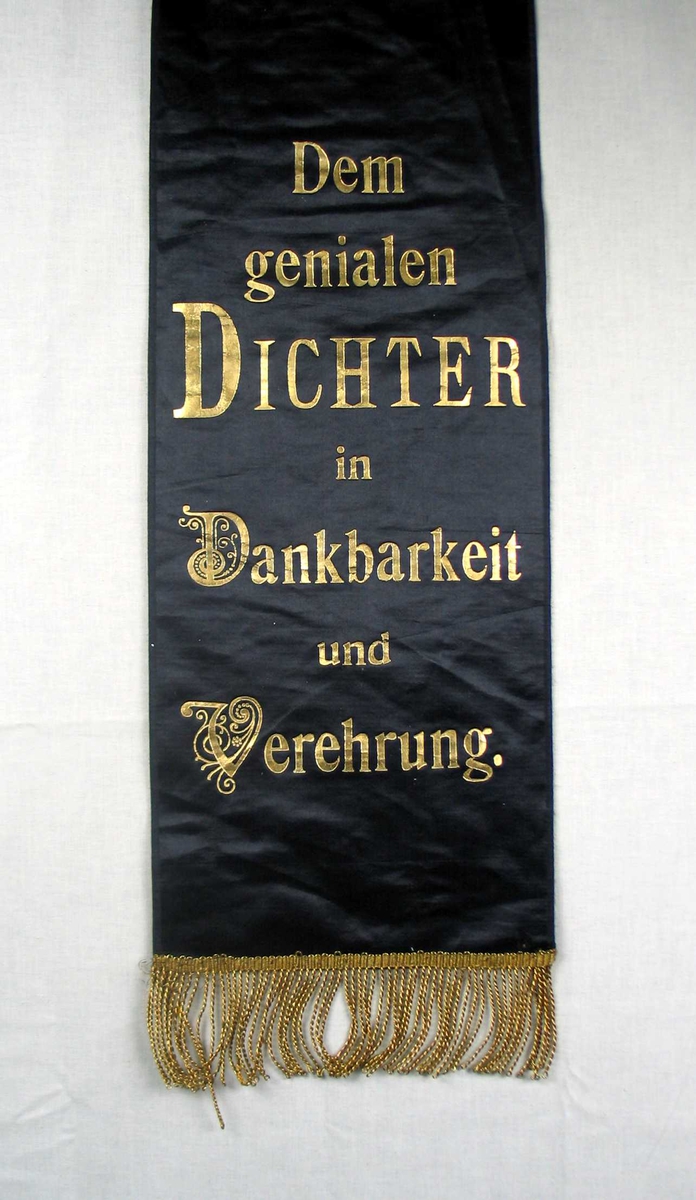 Begravelsessløyfe i svart silke med frynser og tekst i gull.
