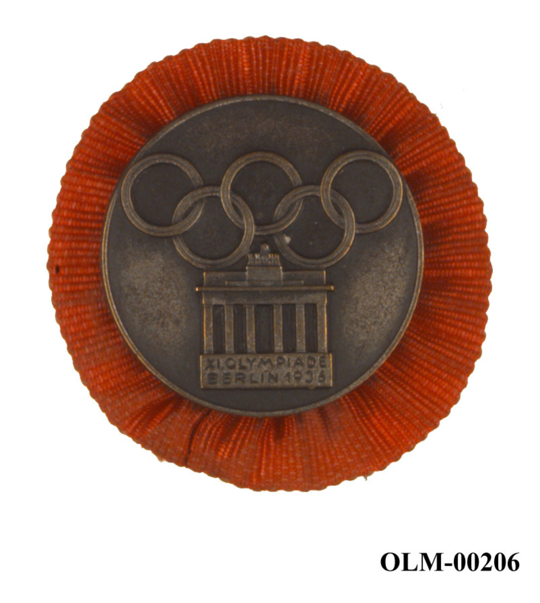 Rundt merke med en form for oransje rosett på baksiden. Merket har motiv av Brandenburg-porten i Berlin og de olympiske ringene. 
