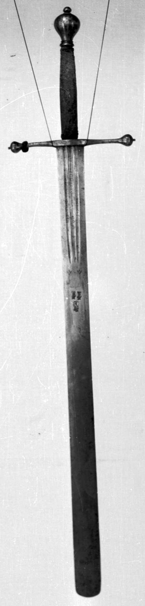 Skarprettersverd.  Pæreformet knapp med fasettetert dekor.
Tregrep viklet med rokkeskinn. 
Rette åttekantede parérstenger som ender i to dråper med kantet dekor. Rett tveegget klinge med ovalt tverrsnitt  og tre korte blodrender på hver side. Innslått tre smedstempler med kronede hoder.  På den ene siden er det gravert inn et hjul og på den andre siden en galge. Begge inngraveringer er innlagt med kobber.

