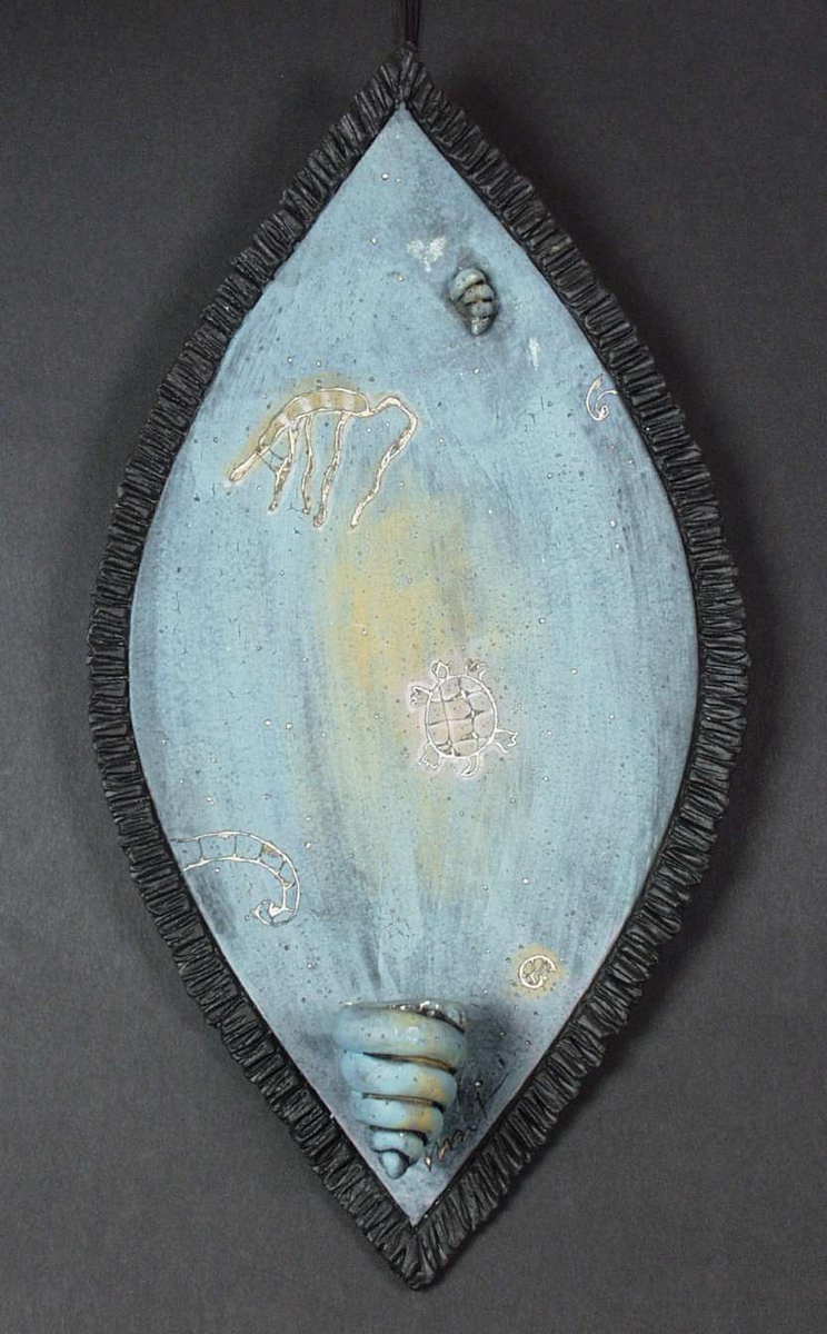 Lysholder i keramikk laget som et skjold der selve lysholderen er spiralformet. Ulike motiv av dyreliv i sjøen er risset inn.