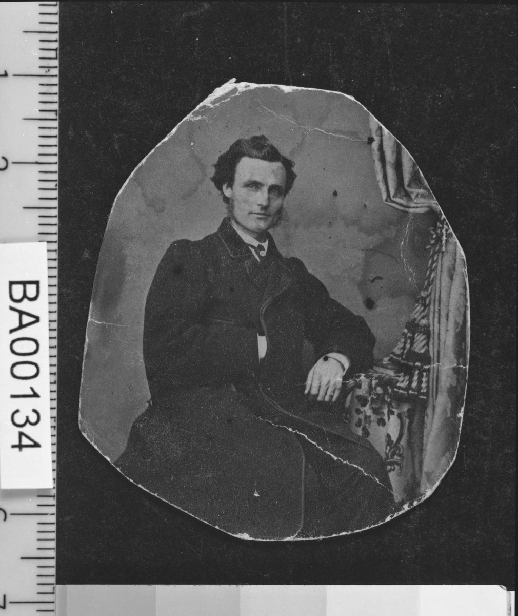 Portrett av yngre mann sittende ved bord og hvilende venstre arm på bordet og høyre hånd i jakken (à la Napoleon); han ser direkte på betrakteren.
