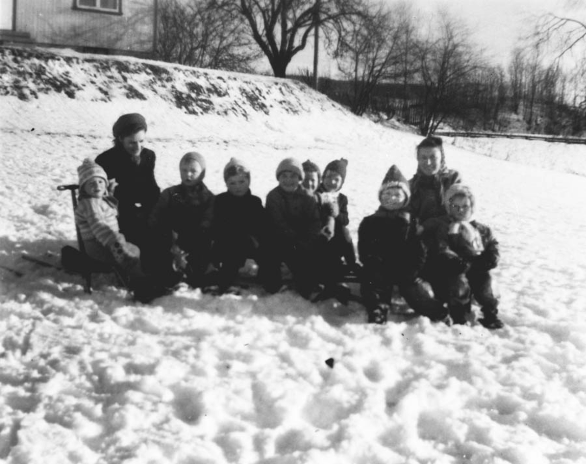 Mange små barn og 2 kvinner i snøen.