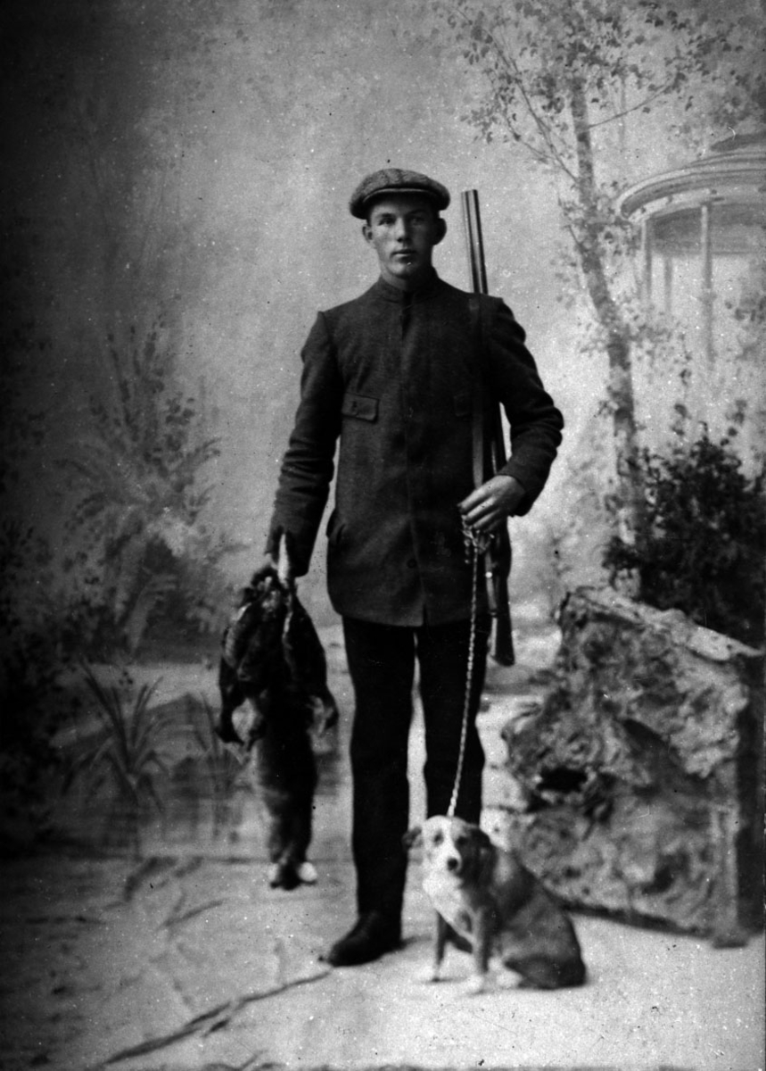 Mann med hund, gevær og jaktbytte. Atelierportrett.