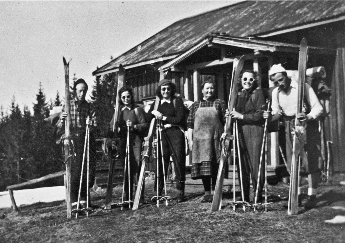 Kvinner og menn med ski utenfor hytte
