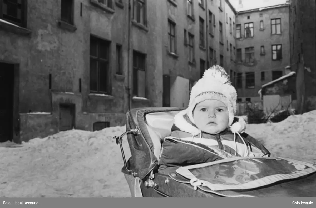 Barn i barnevogn i forfallen bakgård vinterstid. Fotografiet er fra prosjektet og boka ''Oslo-bilder. En fotografisk dokumentasjon av bo og leveforhold i 1981 - 82''. Kontakt Samfoto ved ev. bestilling av kopier.