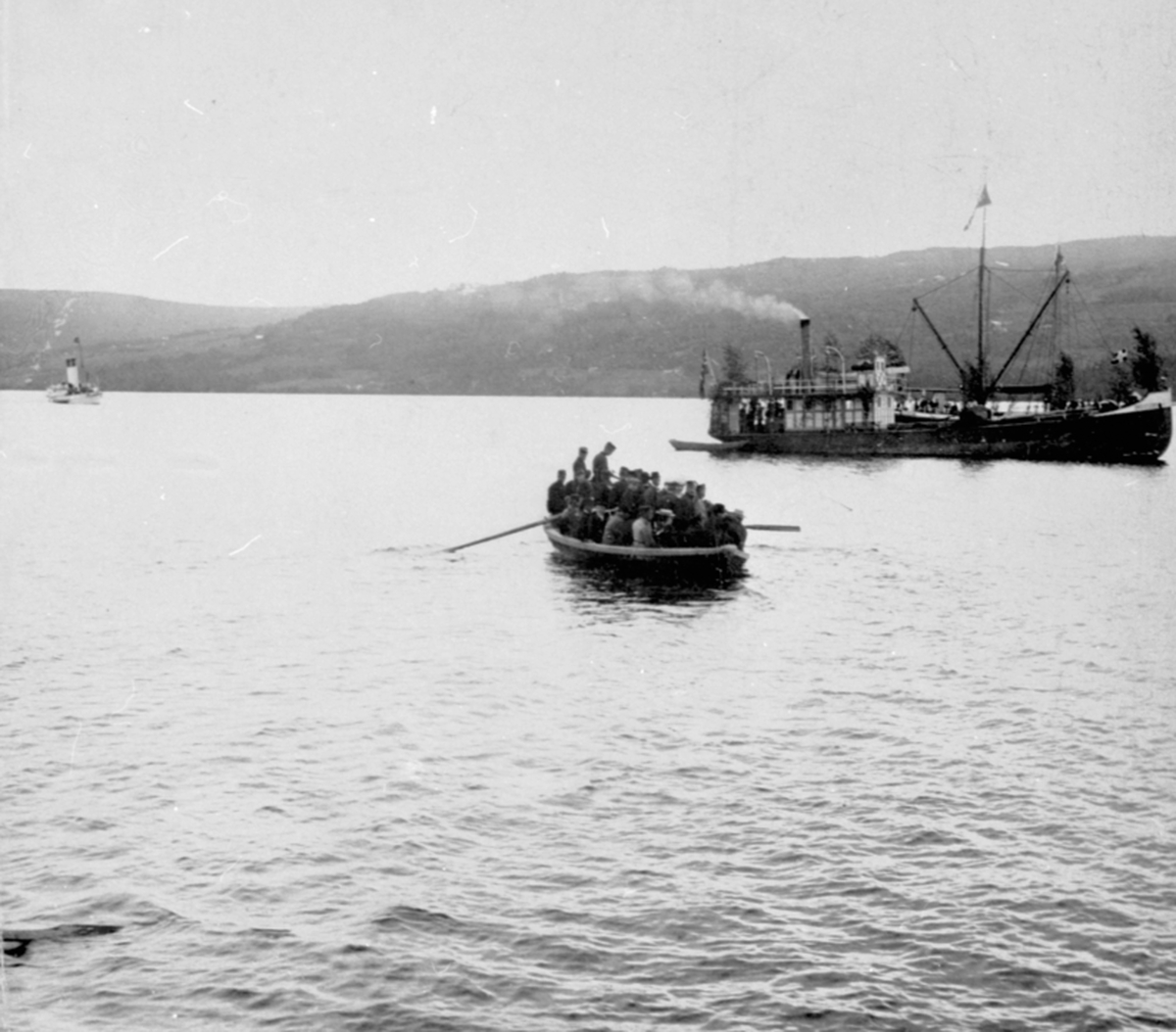 Mjøsbåten D. S. Industri II, pyntet med løv, utenfor Moelv brygge. Robåt full av folk. Kong Oscar i bakgrunnen.