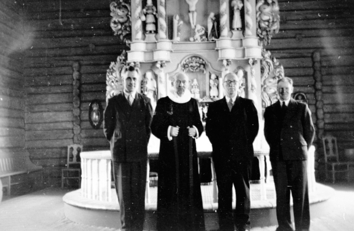 Organist Peder Skjæret, sogneprest Thomas Hauge, kirkesanger Johan Tornes, kirketjener Gunnar Solli foran alteret i Brøttum kirke, Ringsaker.