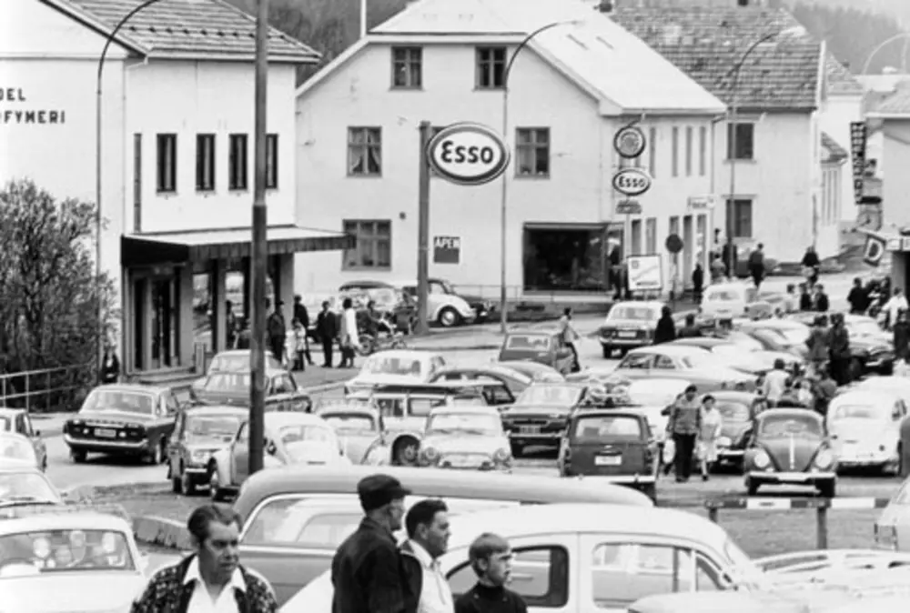 Brumunddal sentrum med trafikk, folk og forretninger langs den gamle riksvegen.