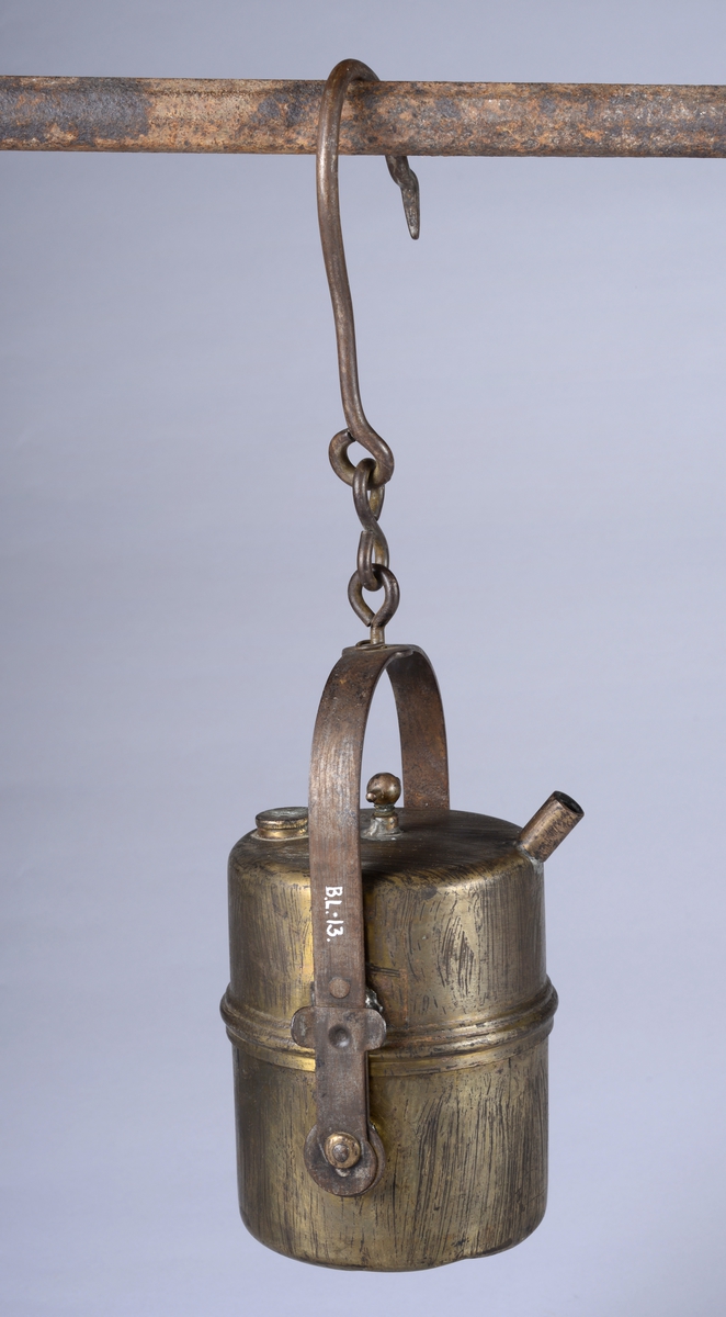 Sylinderformet lampe med håndtak, krokfeste og krok. Tre riller rundt midten av lampen. Et rørstykke på øvre kant av lampen.