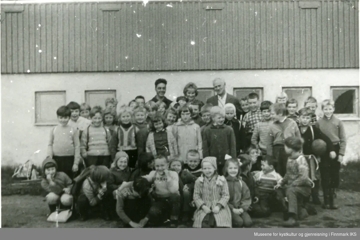 En skoleklasse og tre lärere står oppstil utenfor en skolen i Gamvik.