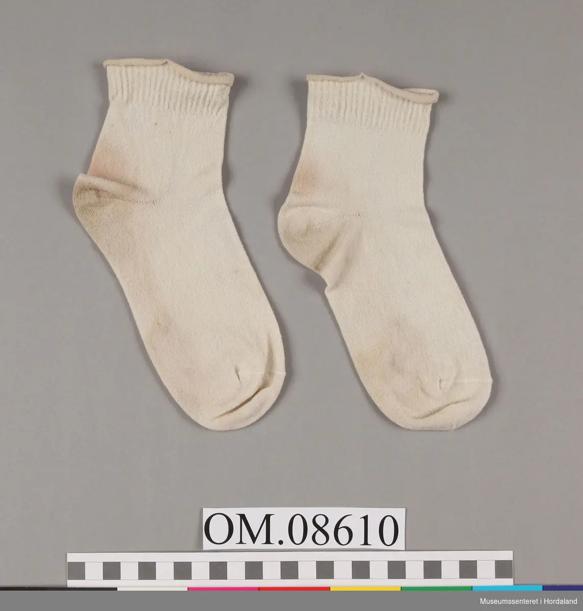 Korte sokkar med smalt brot. Gummistrikken i brotet er utslete. Sokkane har truleg vore kvite, men har farge av lag tids bruk ("skjtten- bege")