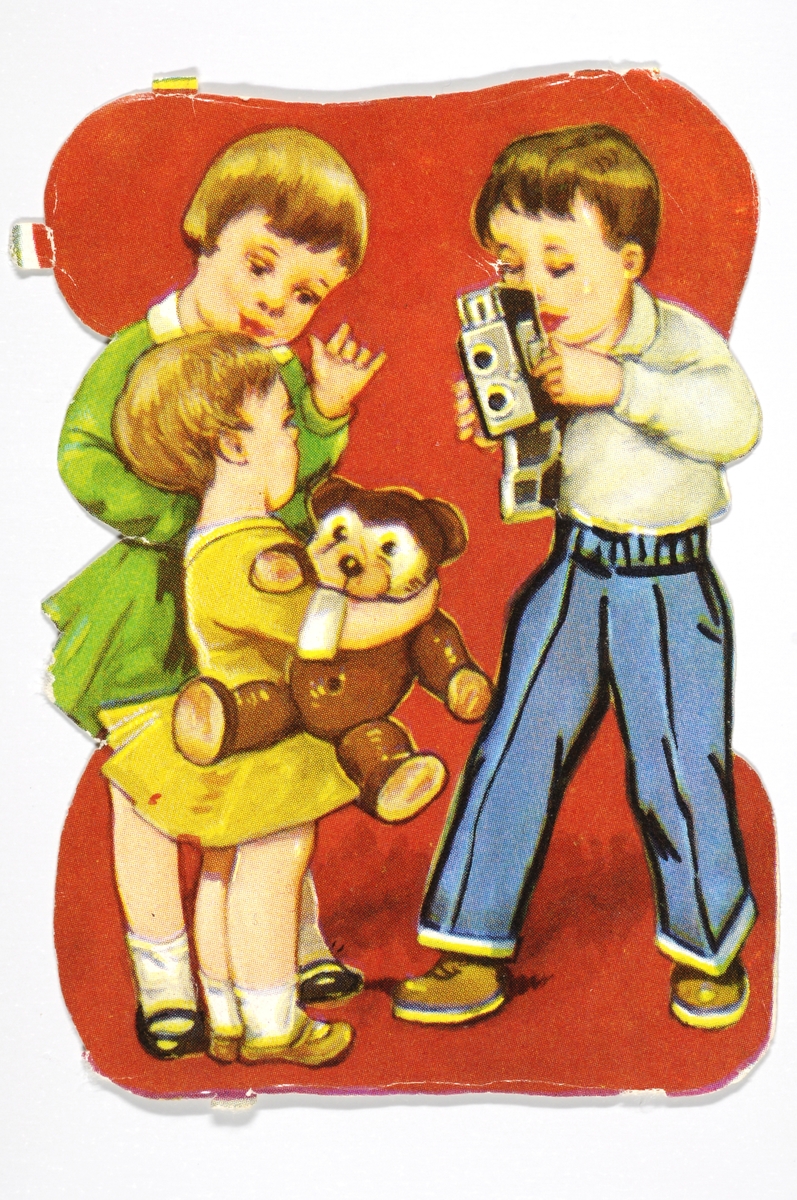 Tre barn hvor en gutt fotograferer. Misnte jenten holder en bamse i hendene.