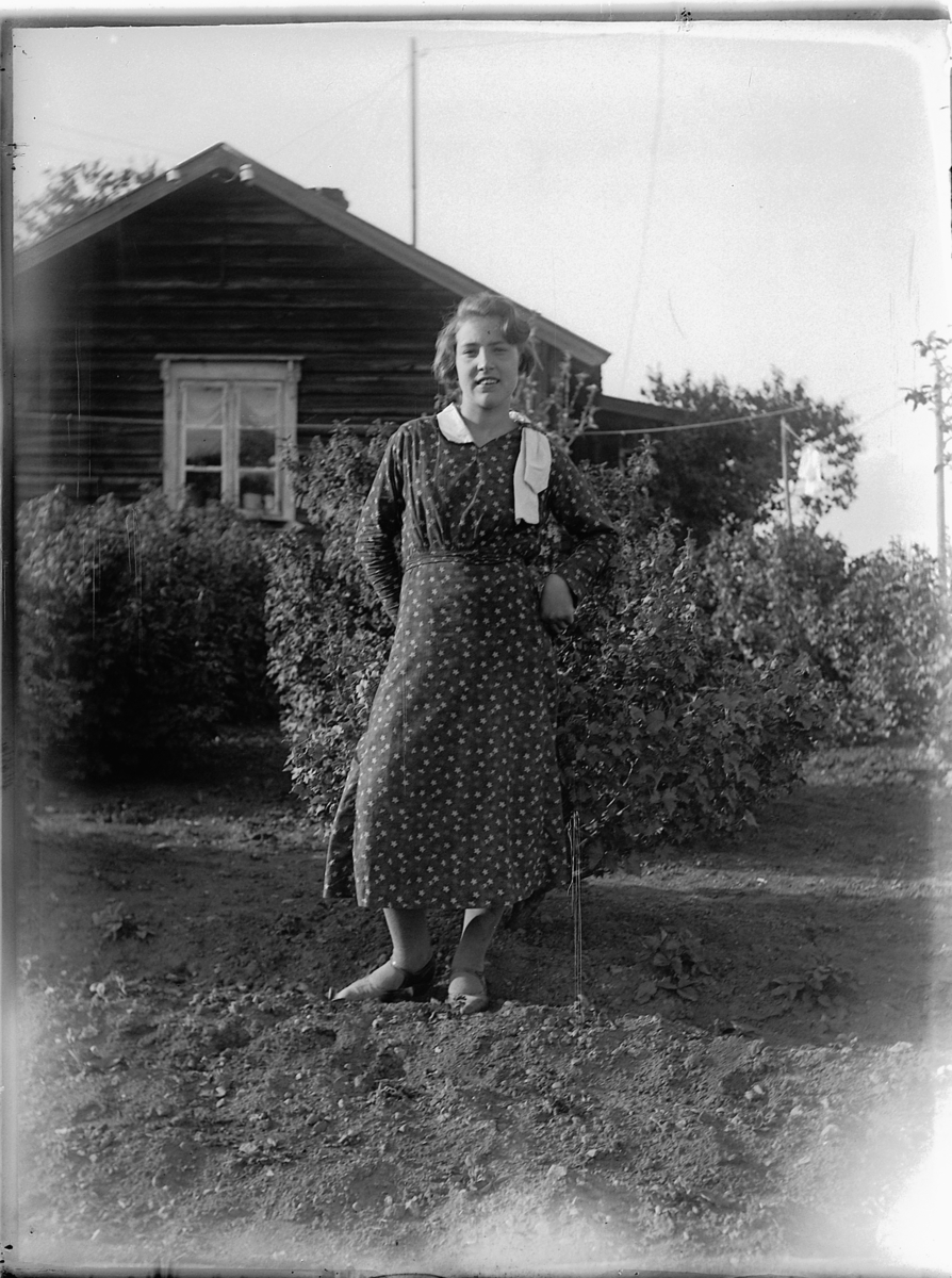 Ukjent kvinne i hagen ved et hus. 