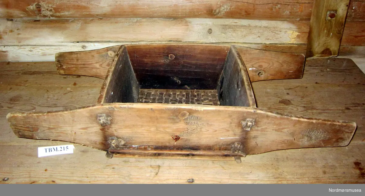 Ein kasse med hankar på kvar side. Hankane er trefjølene som er forlenga. Ein kasse på midten har ein sil laga av spon i botnen.