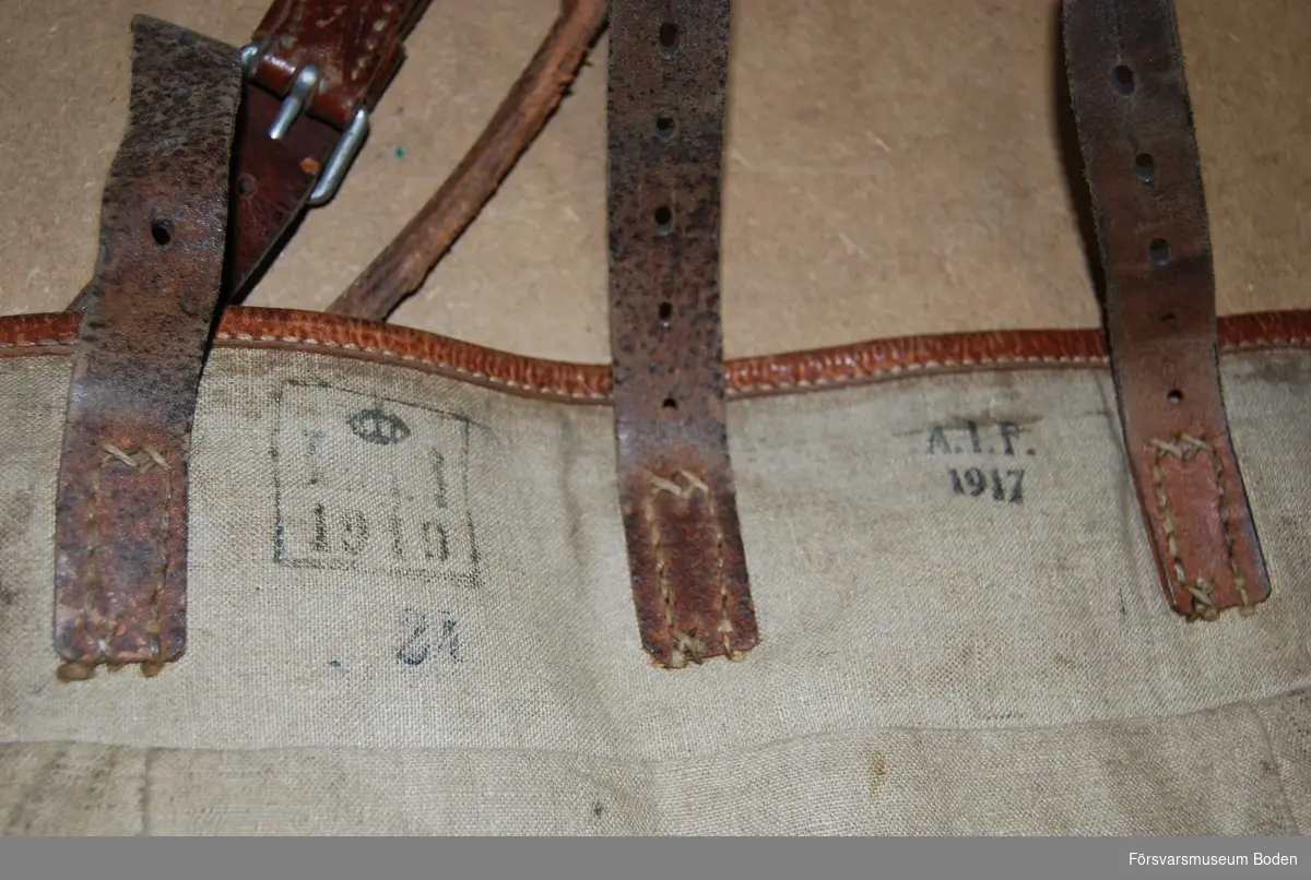 Gråbrunt textilmaterial med läderskodda kanter. Inuti finns en innerficka i locket samt hopsnörbara tygflikar försedda med lädersnören.