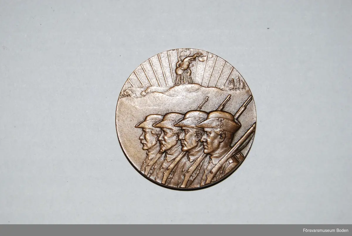 Medalj i brons med korslagda gevär och eklöv med text nedanför på ena sidan, på den andra sidan fyra landstormsmän beväpnade med gevär och i bakgrunden en tänd vårdkase.