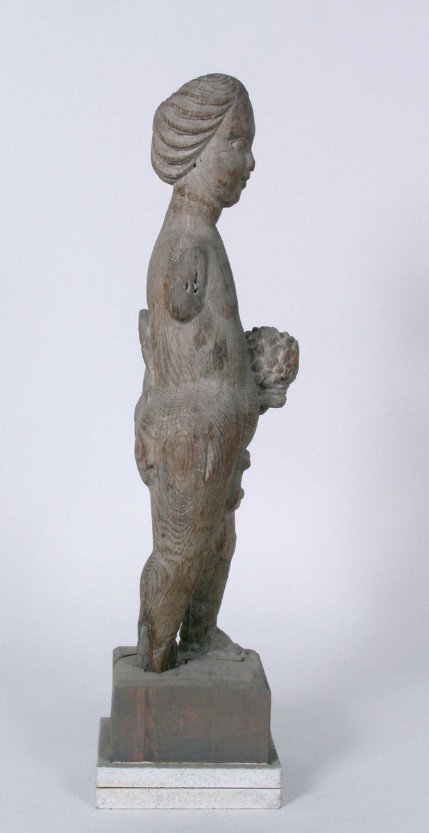 Utskåret trefigur. Det finnes rester av hvit maling i fordypninger (anatkelig linoljemaling. Dertil finnes det et tynt gråhvitt malingslag over hele overflaten. Dette lag er sekundært ettersom det også er påført der deler mangler.