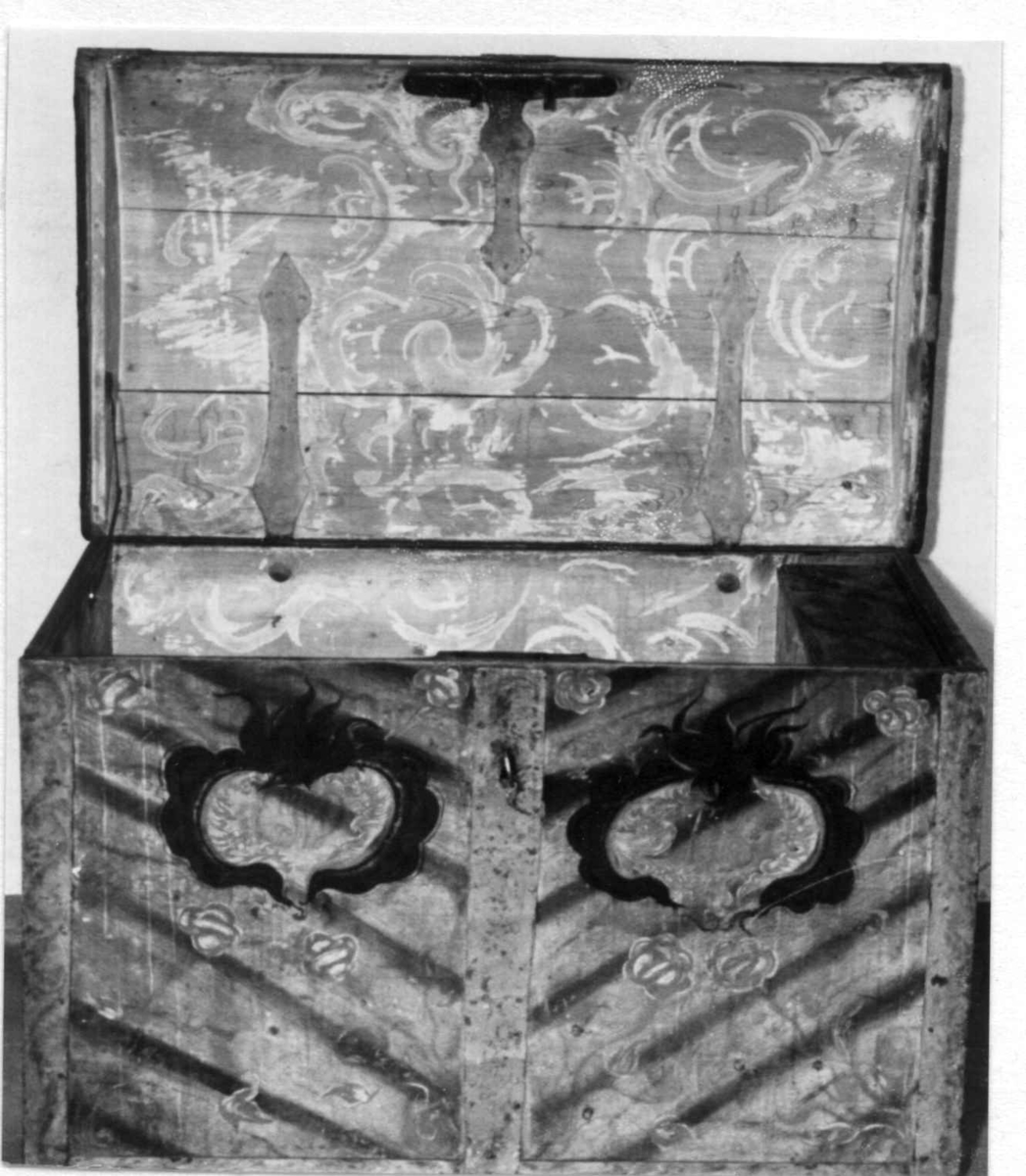 Kiste med buet lokk og smijernsbeslag og bånd. Rosemalt lokk og tre sider. Innvendig rosemaling delvis vasket bort.