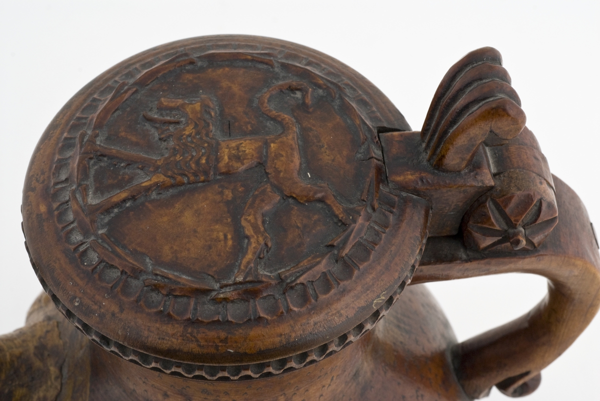 Kanne med skjenketut. Utskåret løve i relieff på lokk, tre ben i form av liggende løver, hvilket tyder på inspirasjon fra løvekanner (Totenkanner).