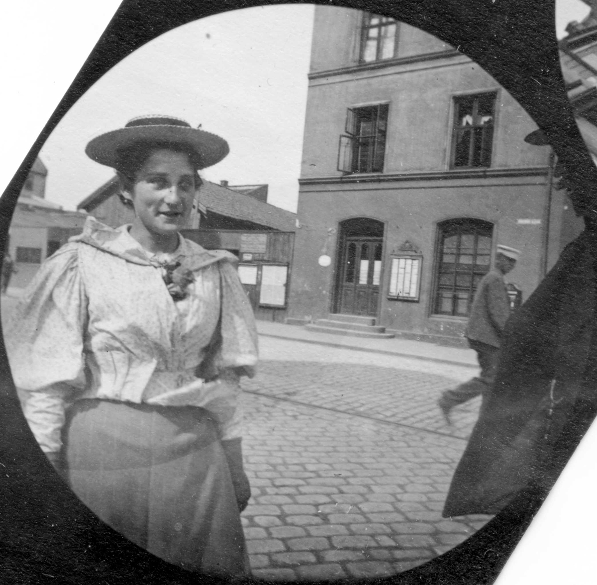 Frk. Collet, senere gift med professor Thue, står i bygate. Mur bygård og lave verkstedsbygninger.