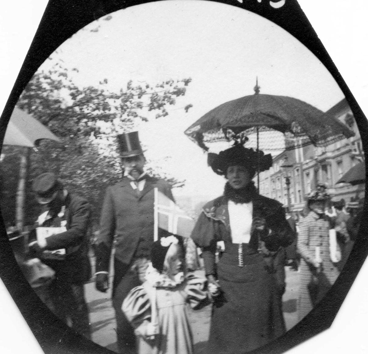 Skuespiller Ludvig Bergh, hans kone Milly (tidligere Thaulow) og datter på Karl Johans gate i Oslo 17. mai,  med norsk flagg, antakelig.Fotografert etter 1906.