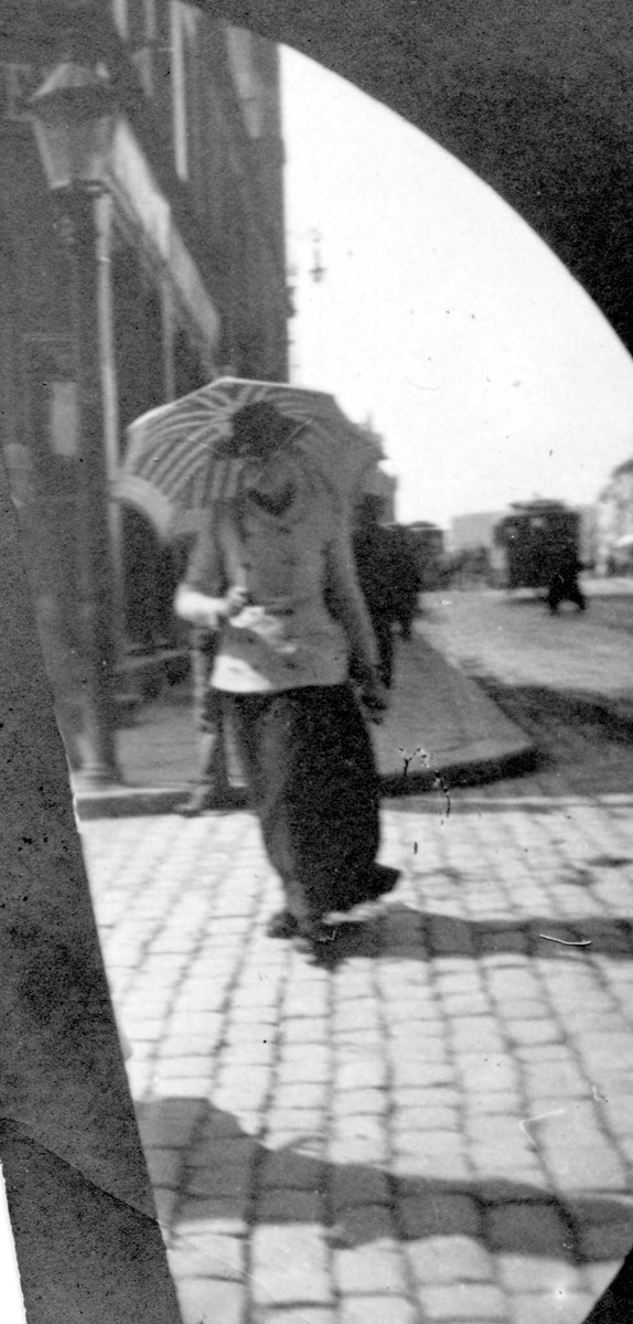 Kvinne med parasoll i bygate, ant. Oslo. Bygårder bak.