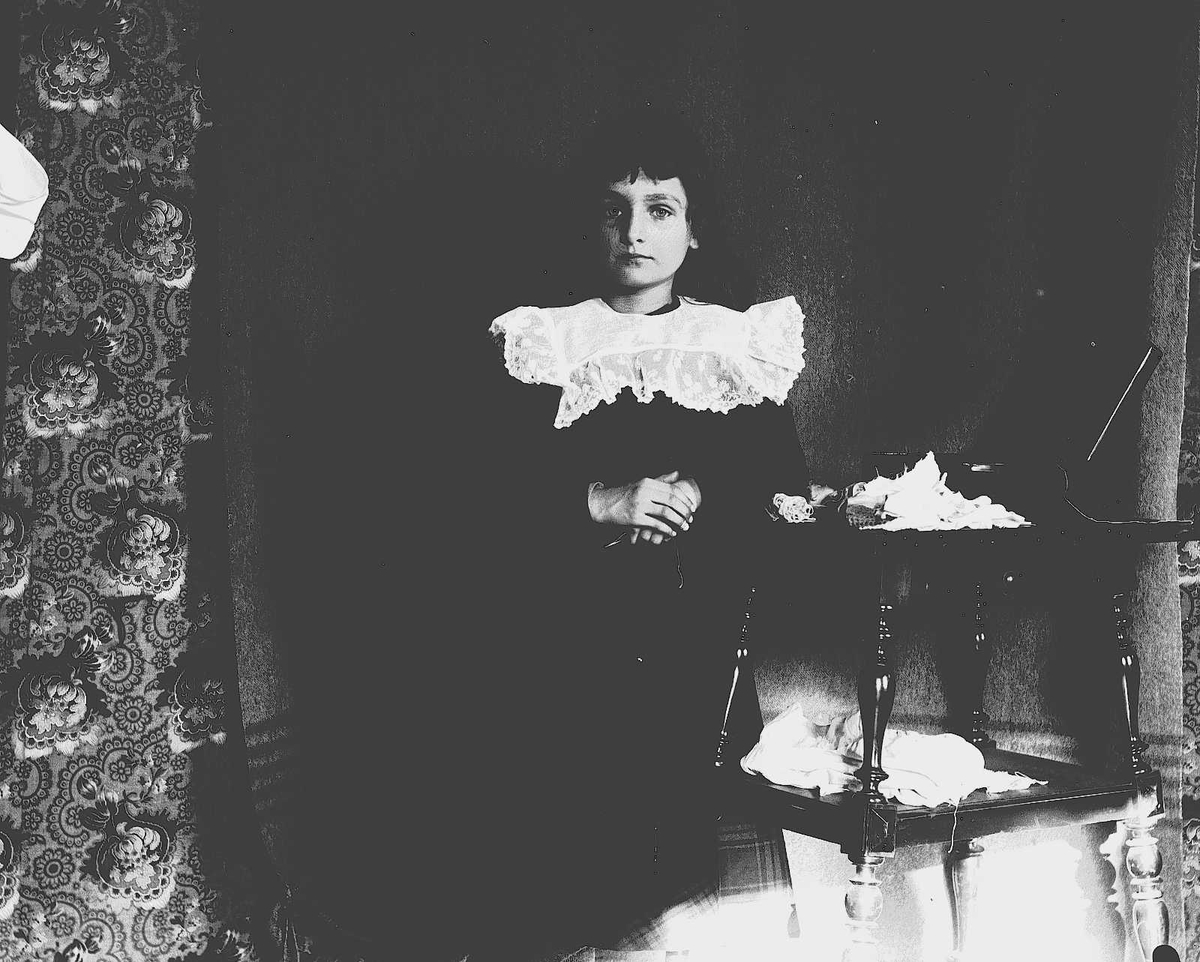 Karen Q.Wiborg står ved et bord, Munkedamsveien 3, Oslo, 1903.