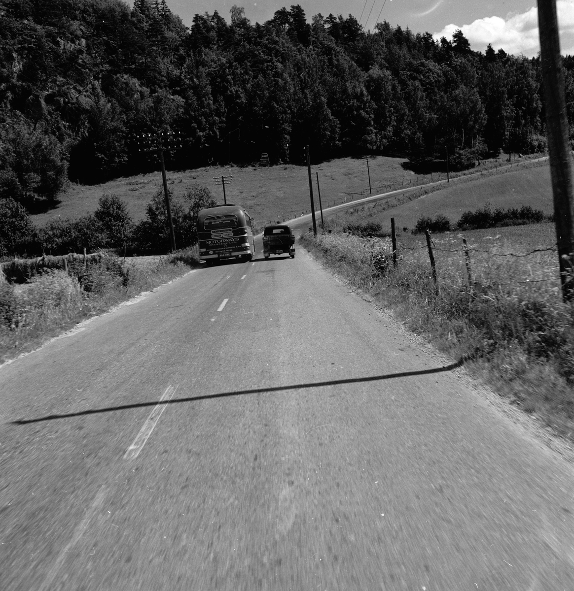 Langs Riksvei 1 kjører det en engelsk turistbuss forbi en norsk lastebil. Fotografert 7. juli 1958.