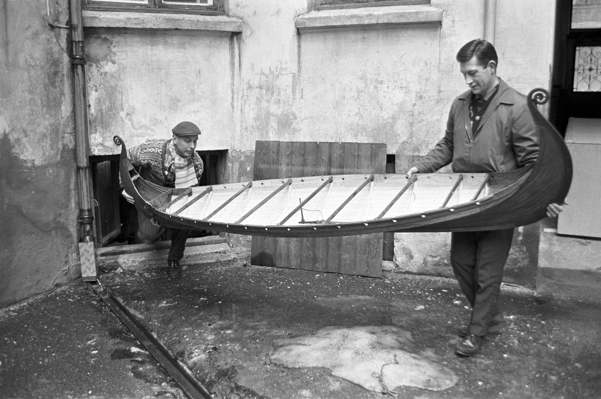 Serie. To menn bærer ut en modell av vikingeskipet "Osebergskipet" av en kjeller. Fotografert 1967.
