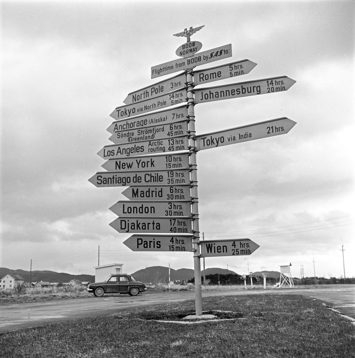 Serie. Et SAS fly står på bakken på Bodø flyplass, mange flydestinasjoner står på et skilt ved Bodø flyplass og en skjære bygger reir på en telefonstolpe. Fotografert april 1963.
