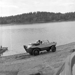 Serie. En kvinne og en mann sitter i en amfibiebil av typen 