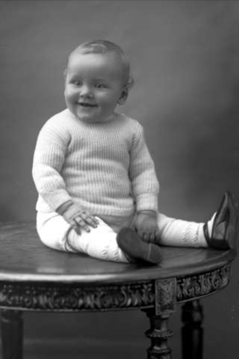 Portrett, barn i strikkegenser sitter på et bord. Tannlege Holmbech Hansens sønn.