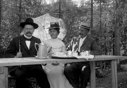 Gruppe på tre sittende ved dekket bord utendørs. Avfotografe