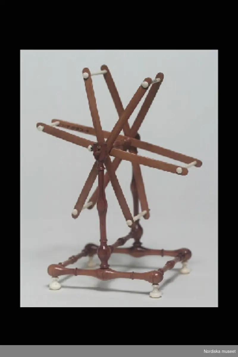 Inventering Sesam 1996-1999
H 13,5    B 7   (cm)
Nystvinda, leksak, av brunt, svarvat och polerat trä, kvadratisk fotställning med kulfötter av ben, vinda med 6 st armar och detaljer i ben.
Birgitta Martinius 1997