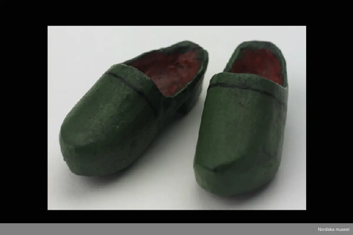 Inventering Sesam 1996-1999:
L 5,5 cm
Ett par träskor, helt snidade i trä, utsidan målad grön, insidan röd.
Troligen dockskor eller souvenir.
Leif Wallin 1996