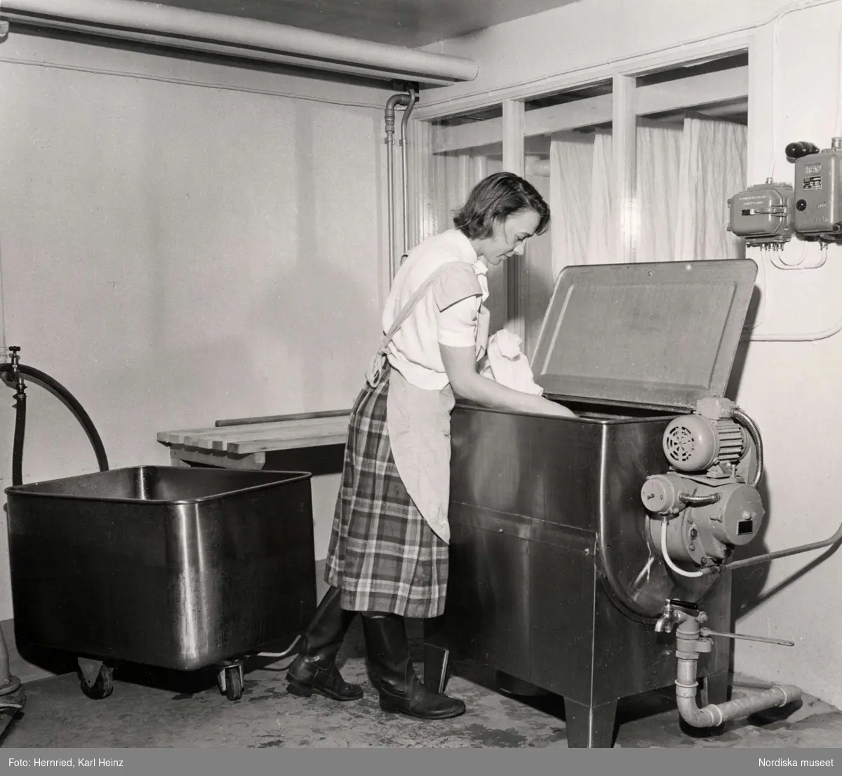 Nockebyhov, Uppland. Kvinna i tvättstuga. Lägger tvätt i toppmatad tvättmaskin