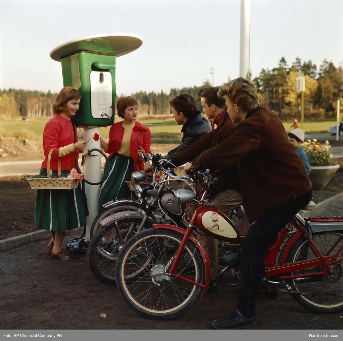 BP-mack. Tre ynglingar på mopeder och två "blomsterflickor" vid bensinstation.