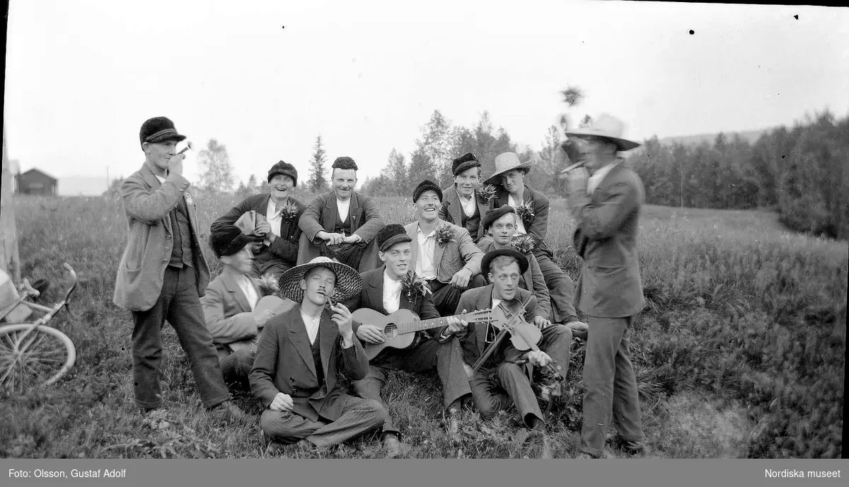 En grupp unga män med musikinstrument i grässlänt. Början av 1900-talet.