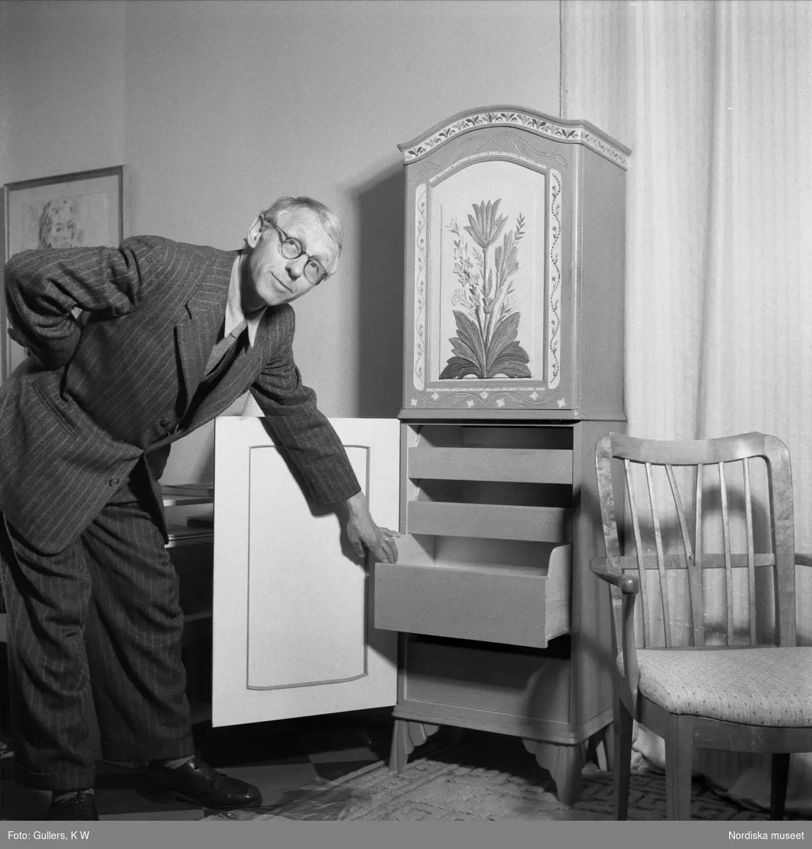 Professor Carl Malmsten, möbelformgivare och inredningsarkitekt, drar ut låda i skåp i allmogestil.