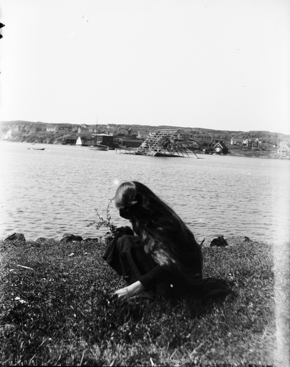 Flicka plockat blommor på strand. I bakgrunden torkställning för fisk eller nät. Fiskebäckskil, Bohuslän.